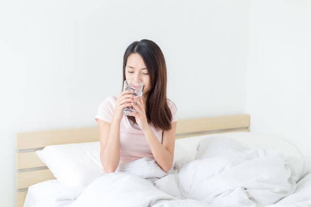 ベッドで水を飲む女性